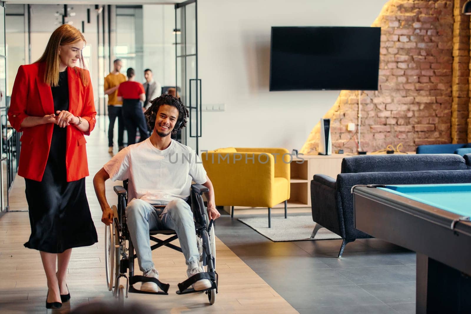 A diverse group of young professionals, including businesswomen and an African-American entrepreneur in a wheelchair, engage in collaborative discussion on various business projects in a modern startup office setting