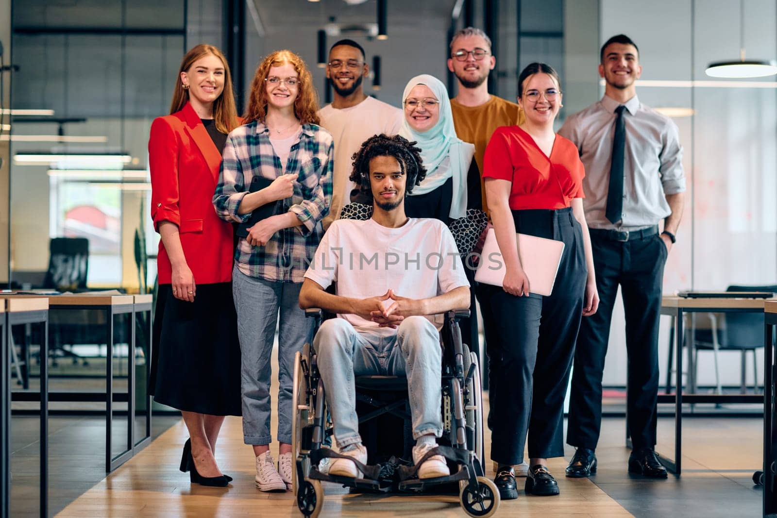 A diverse group of young business people walking a corridor in the glass-enclosed office of a modern startup, including a person in a wheelchair and a woman wearing a hijab by dotshock