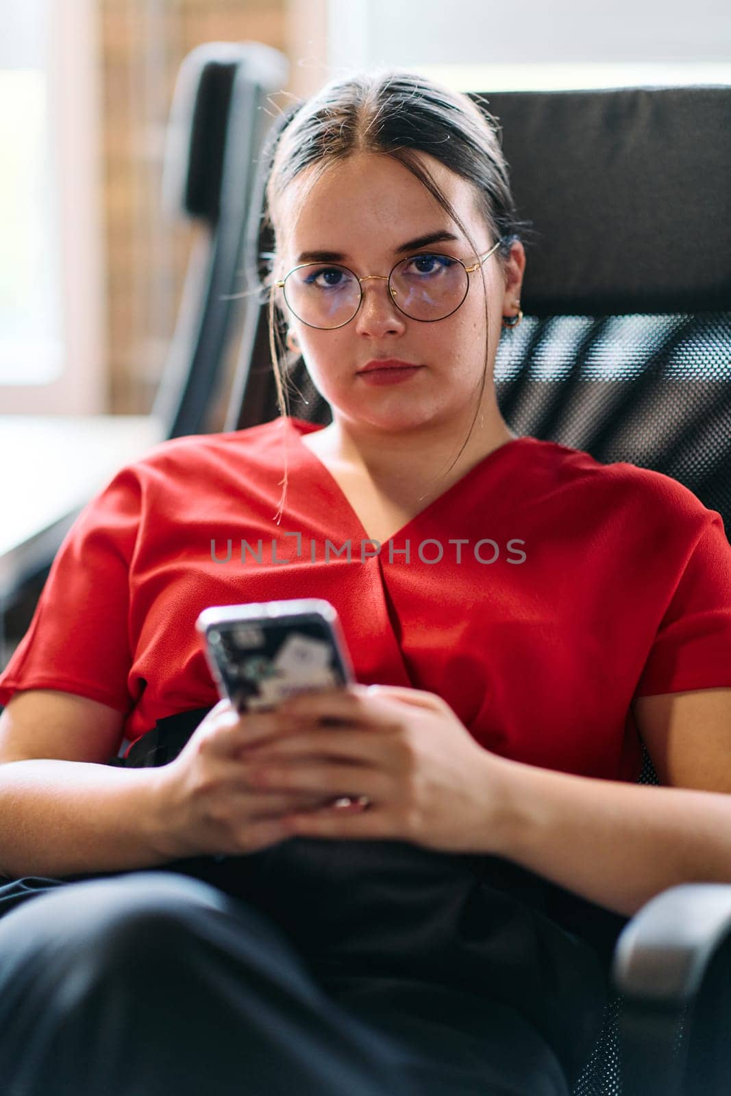 A businesswoman resting on a short break from work in a modern startup coworking center, using her smartphone to unwind and recharge by dotshock