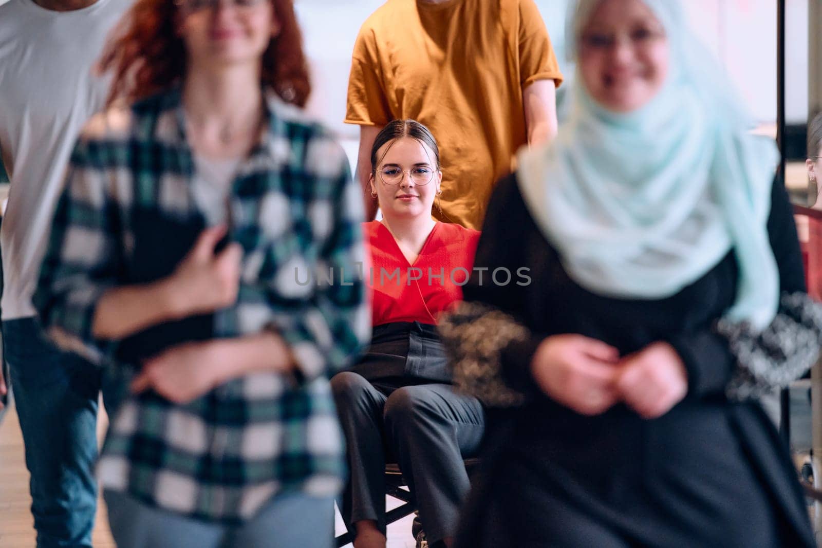 people walking a corridor in the glass-enclosed office of a modern startup, including a person in a wheelchair and a woman wearing a hijab.