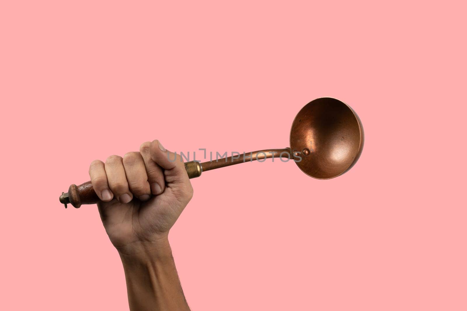 Black male hand holding a brass vintage kitchen ladle isolated on pink background by TropicalNinjaStudio