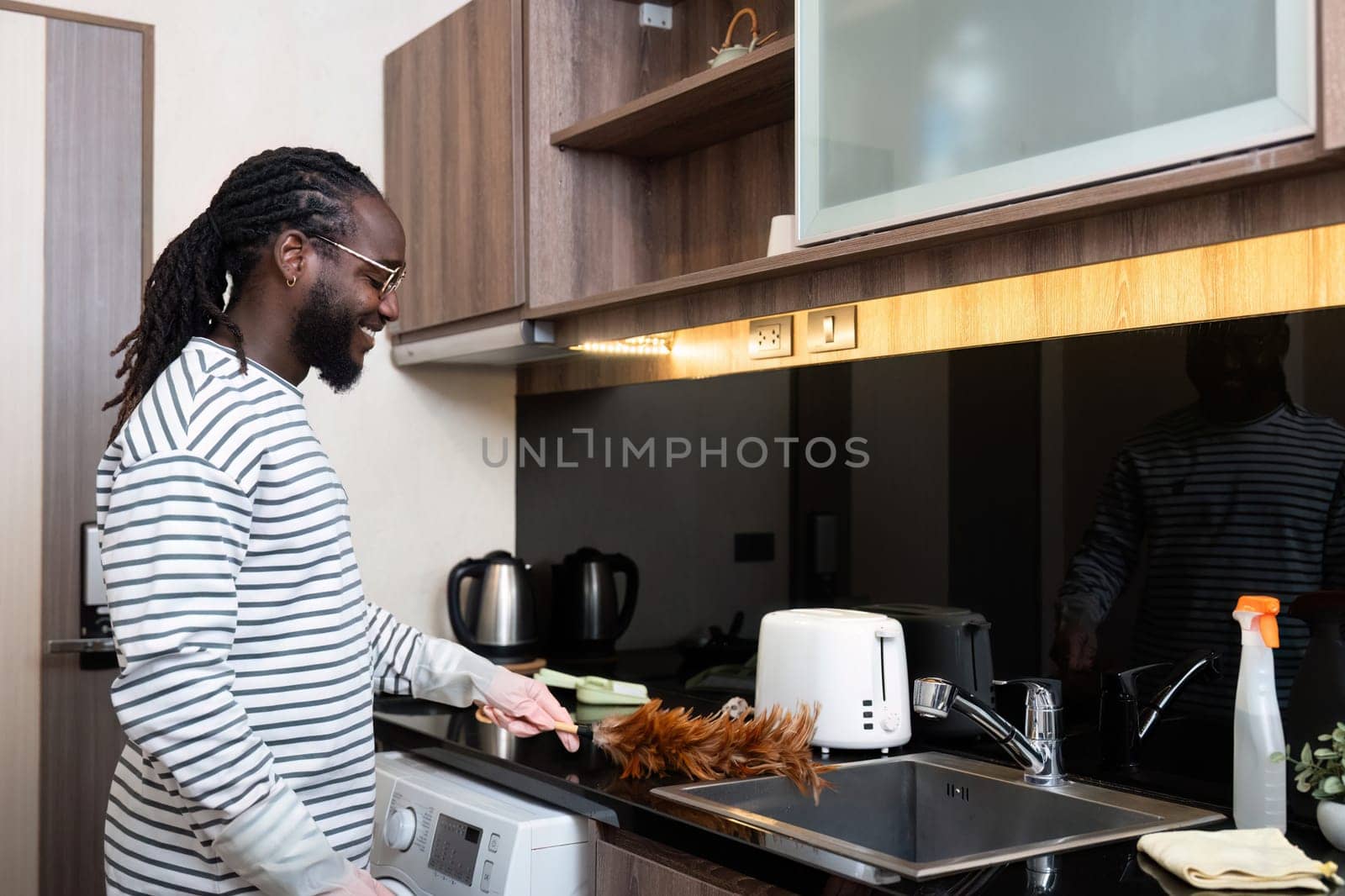 African American man young use duster cleaning in kitchen at home.