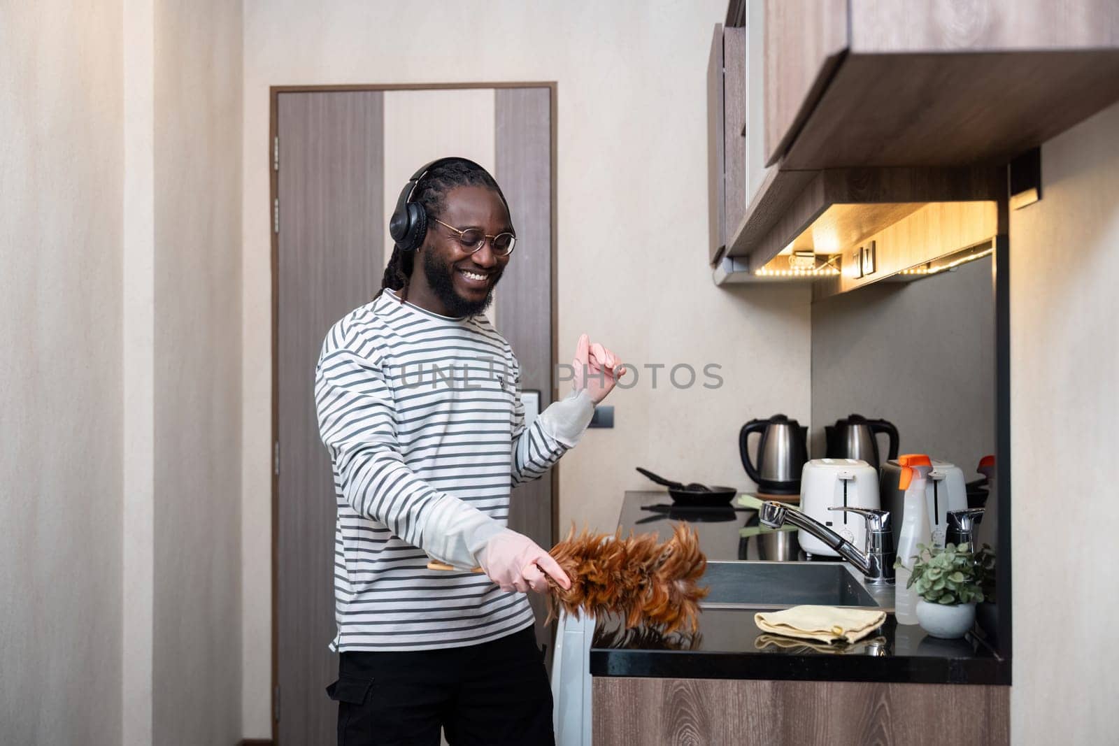 African American man listening to music while cleaning in kitchen by nateemee