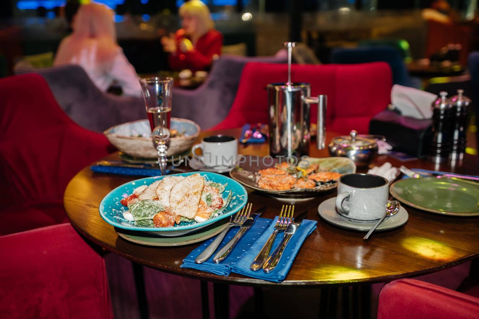 A table with a blue plate of salad and a cup of coffee. The table is set with silverware and a few cups. Scene is casual and inviting, as it is a restaurant setting with people enjoying their meals. by Matiunina