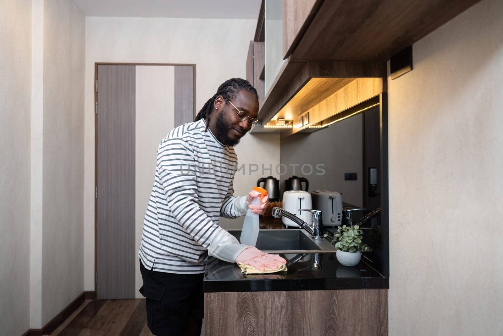 African American man in rubber gloves wipe dust from table in kitchen, Housework, cleaning, lifestyle, household by nateemee