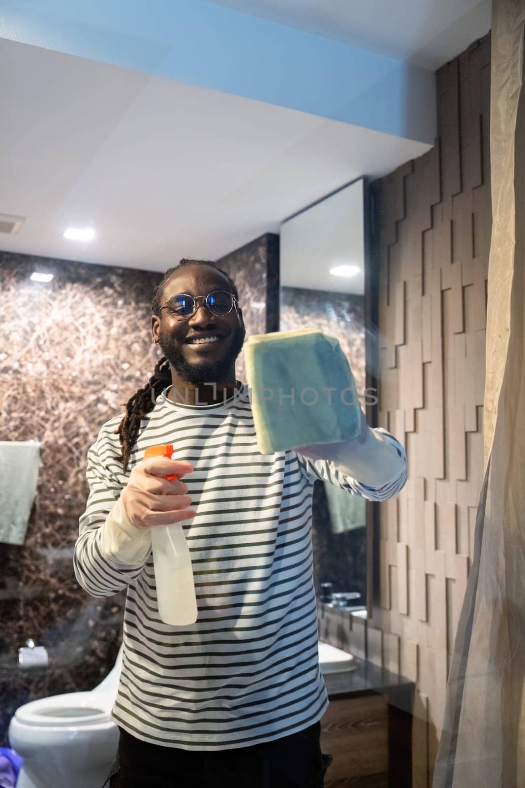 Happy young African American man cleaning the glass in the apartment. Cleaning maintain cleanliness in with towel and spray detergent by nateemee