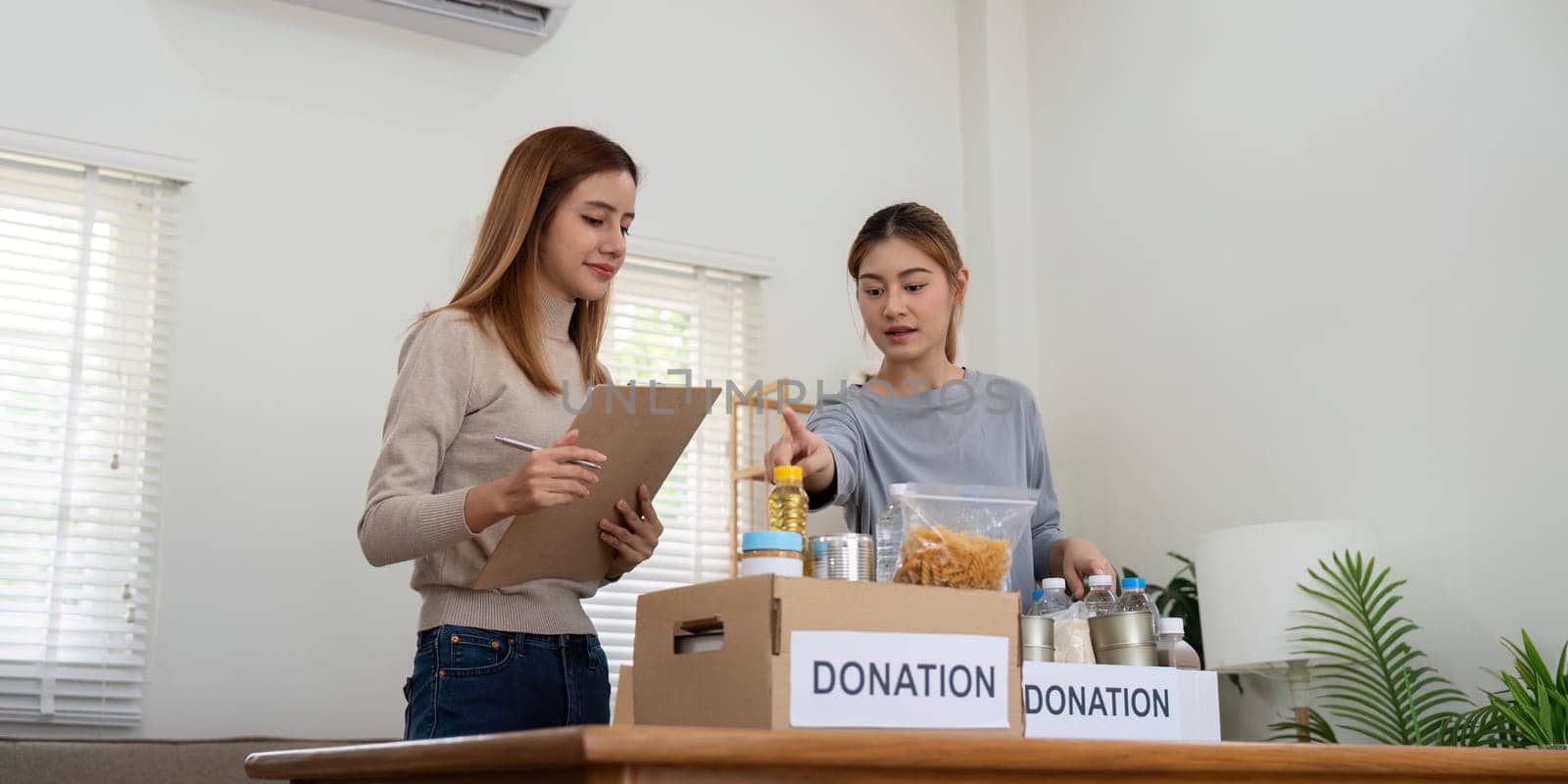 Donation and two woman volunteer asian of happy packing food in box at home. Charity by nateemee