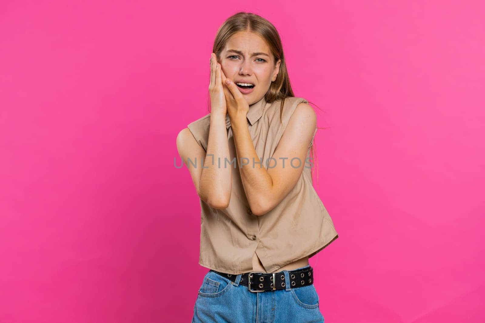Dental problems. Young woman touching cheek, closing eyes with expression of terrible suffer from painful toothache, sensitive teeth, cavities. Pretty blonde girl isolated on pink studio background