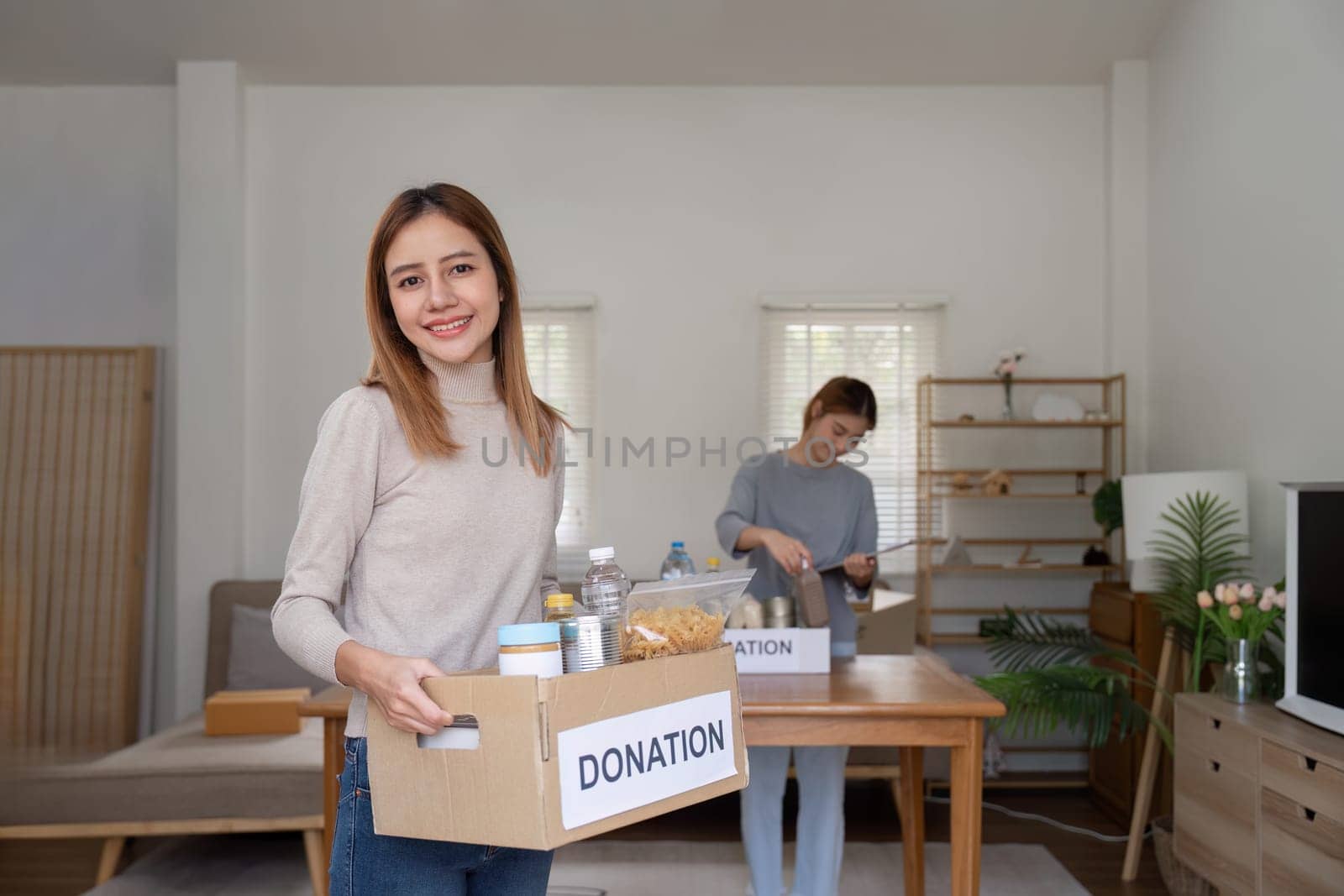 Woman with charity box and group of volunteers at assistance center. Charity, donation, and volunteering concept.