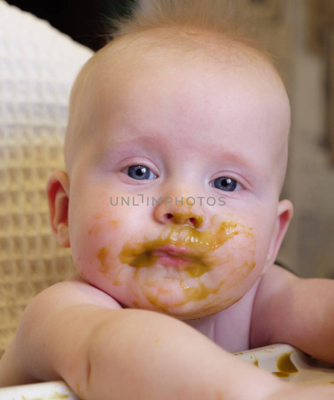 Mom feeding little boy with broccoli puree. Child at the age of six months eats broccoli while sitting on a baby chair.