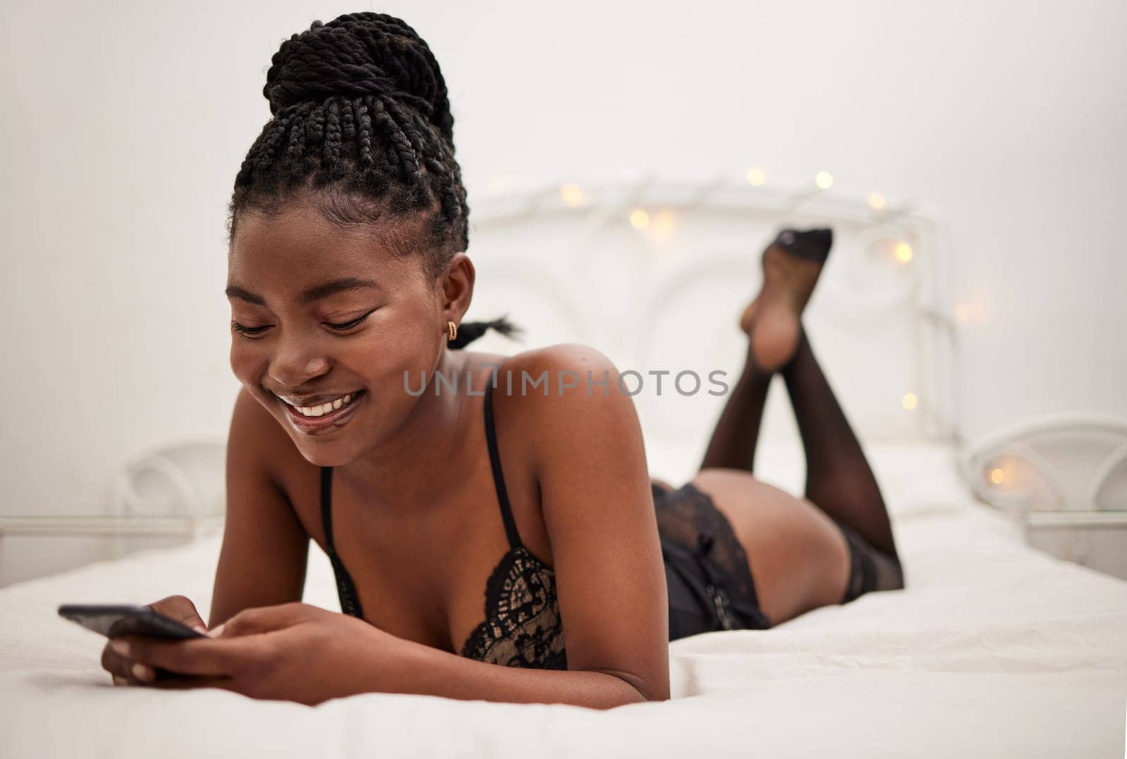 Lingerie, woman and smartphone in bed for texting, messaging and social media with smile at chat. Sexy, black person and mobile communication in underwear for sexting, romance and flirting online.
