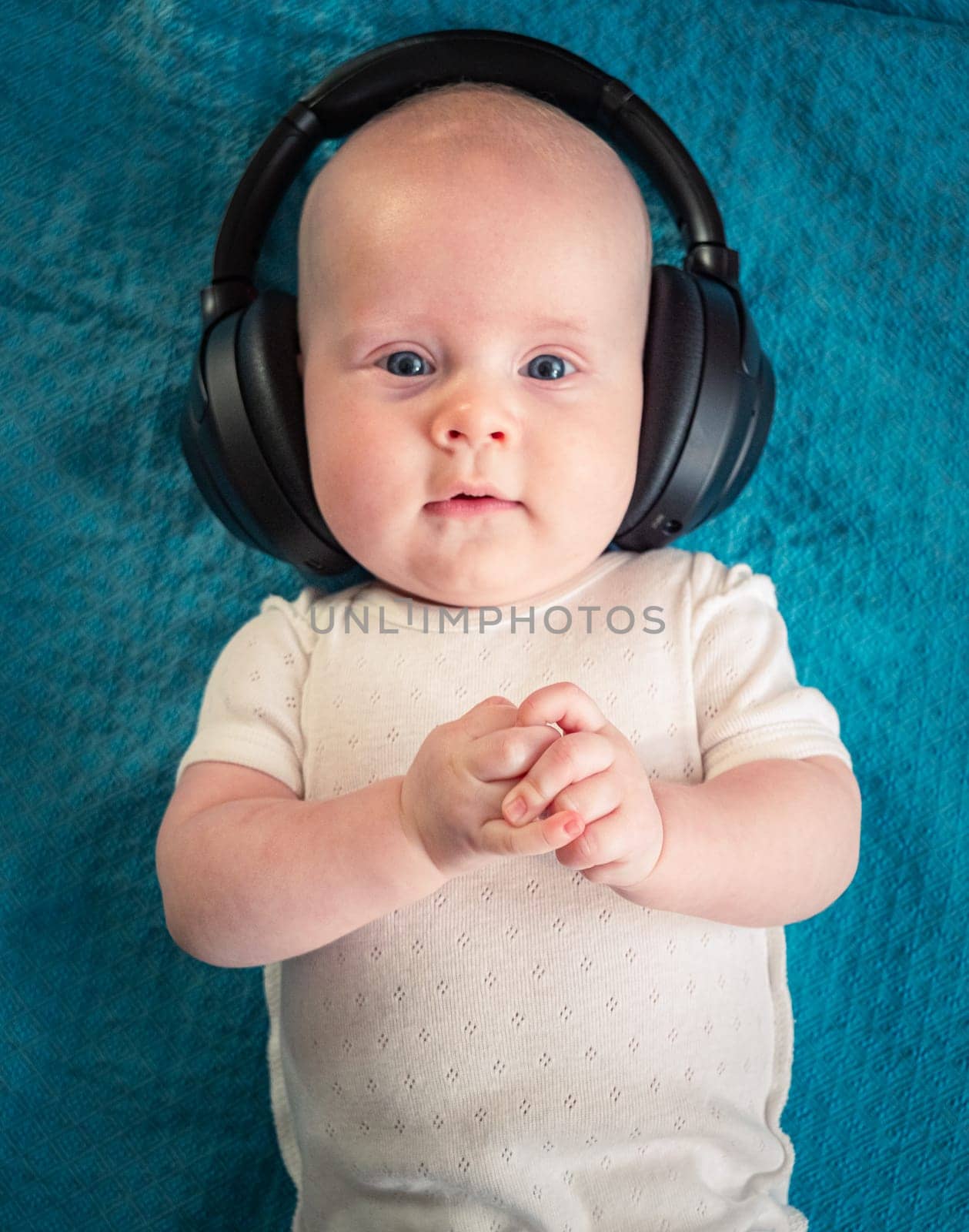 Little boy on blue blanket background with black wireless headphones by Busker