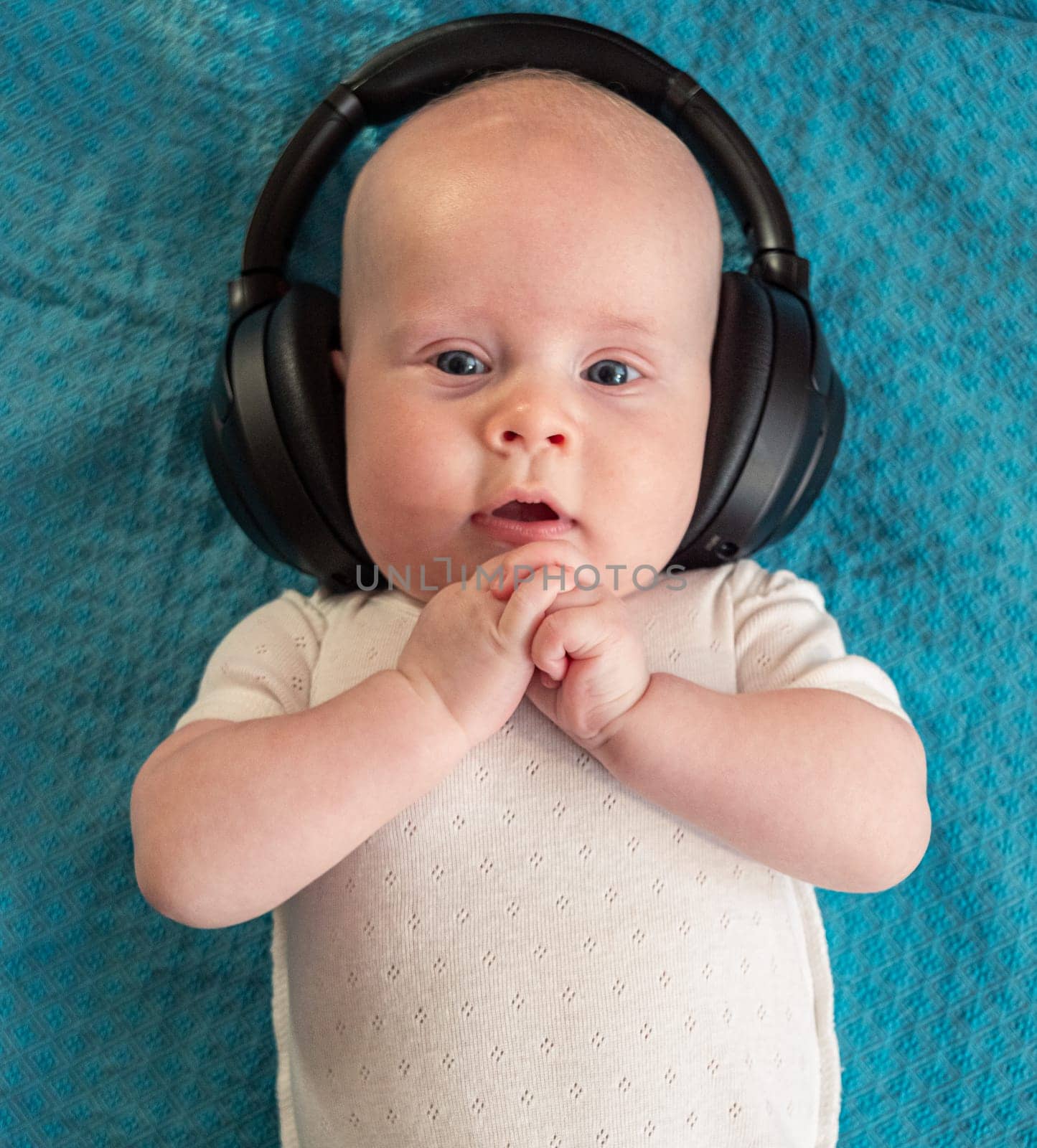 Little boy on blue blanket background with black wireless headphones by Busker