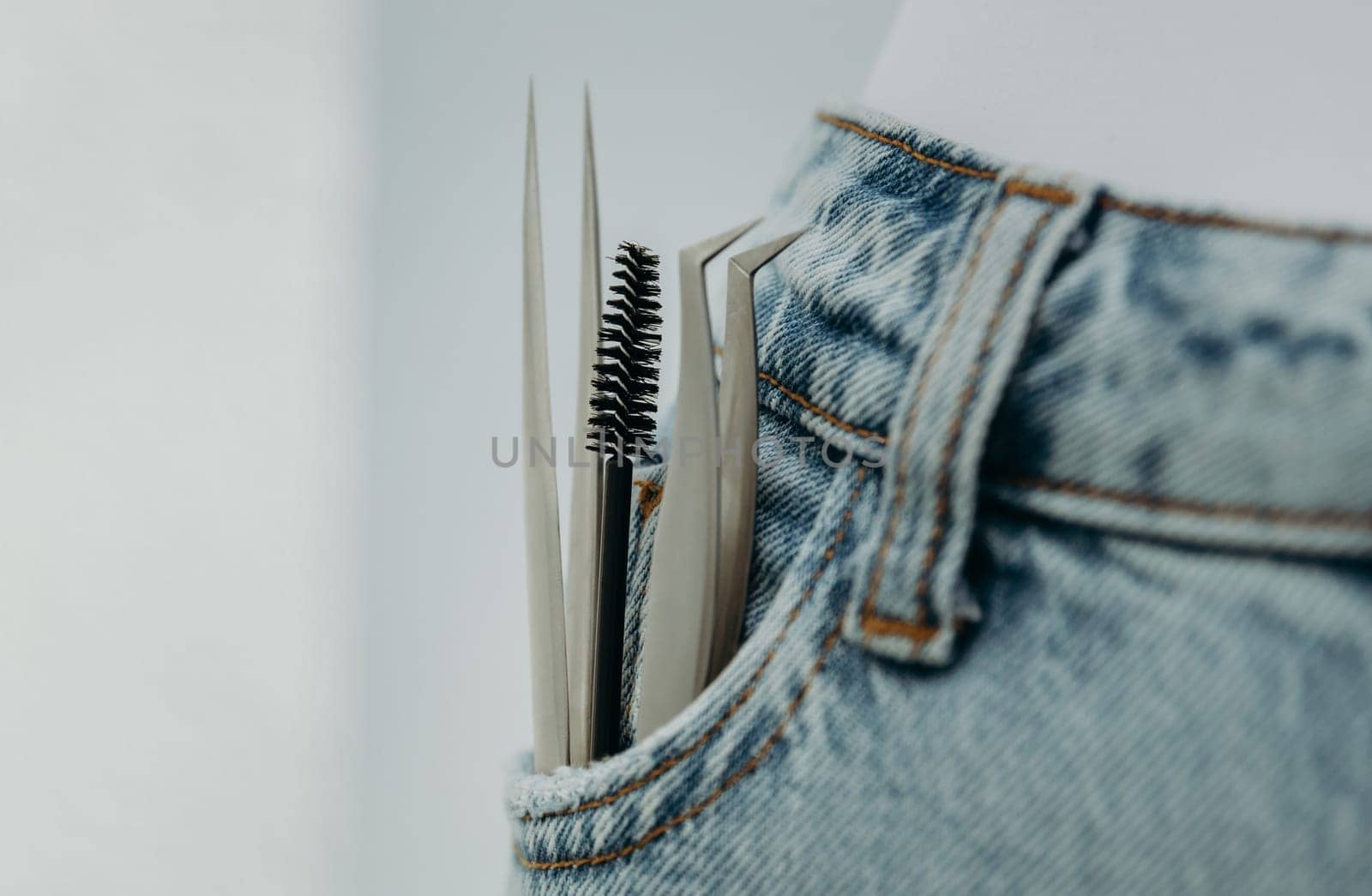 Two tweezers and a brush for eyelash extensions in a jeans pocket. by Nataliya