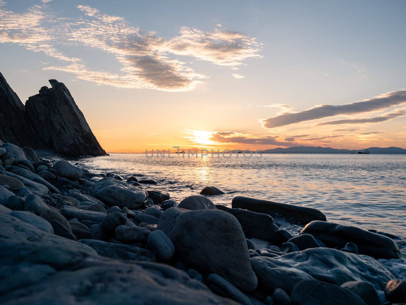 Romantic soft sunrise over the seacoast. Epic summer seascape with clouds floating in the sky and waves crashing to the shore.