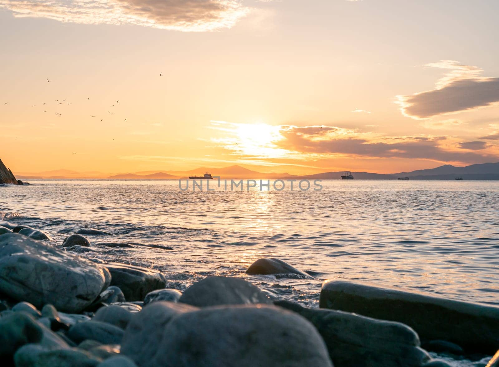 Romantic soft sunrise over the seacoast. Epic summer seascape with clouds floating in the sky and waves crashing to the shore.