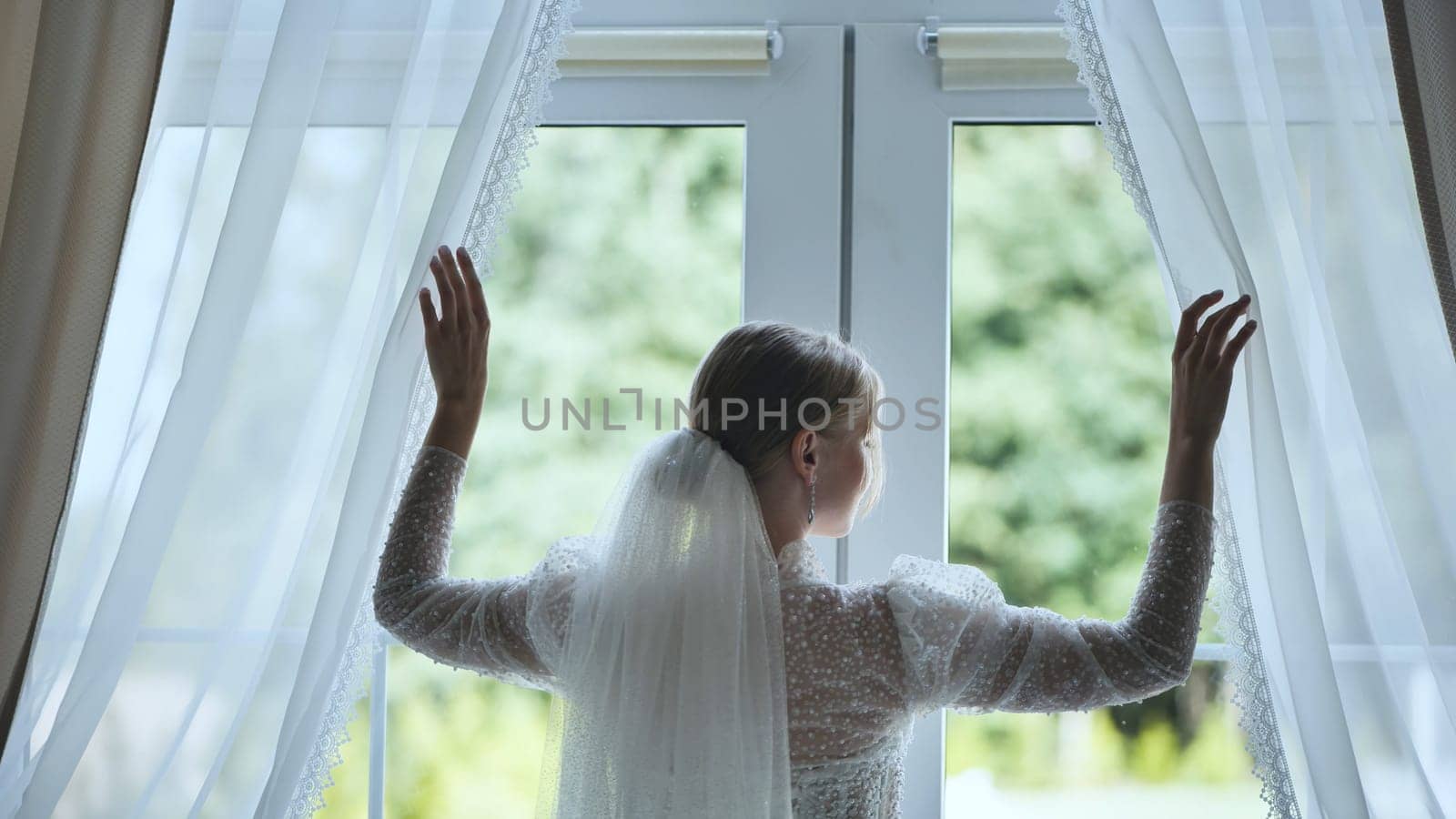 The bride adjusts the curtains at the window