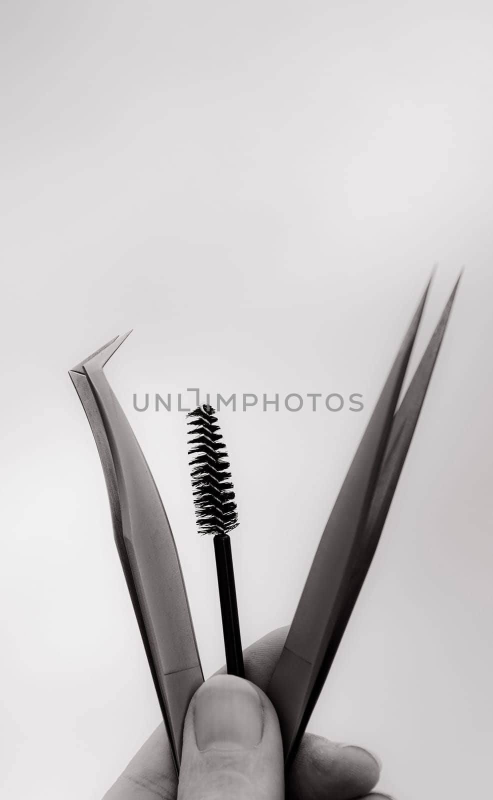 A hand holds two tweezers and a brush for eyelash extensions. by Nataliya