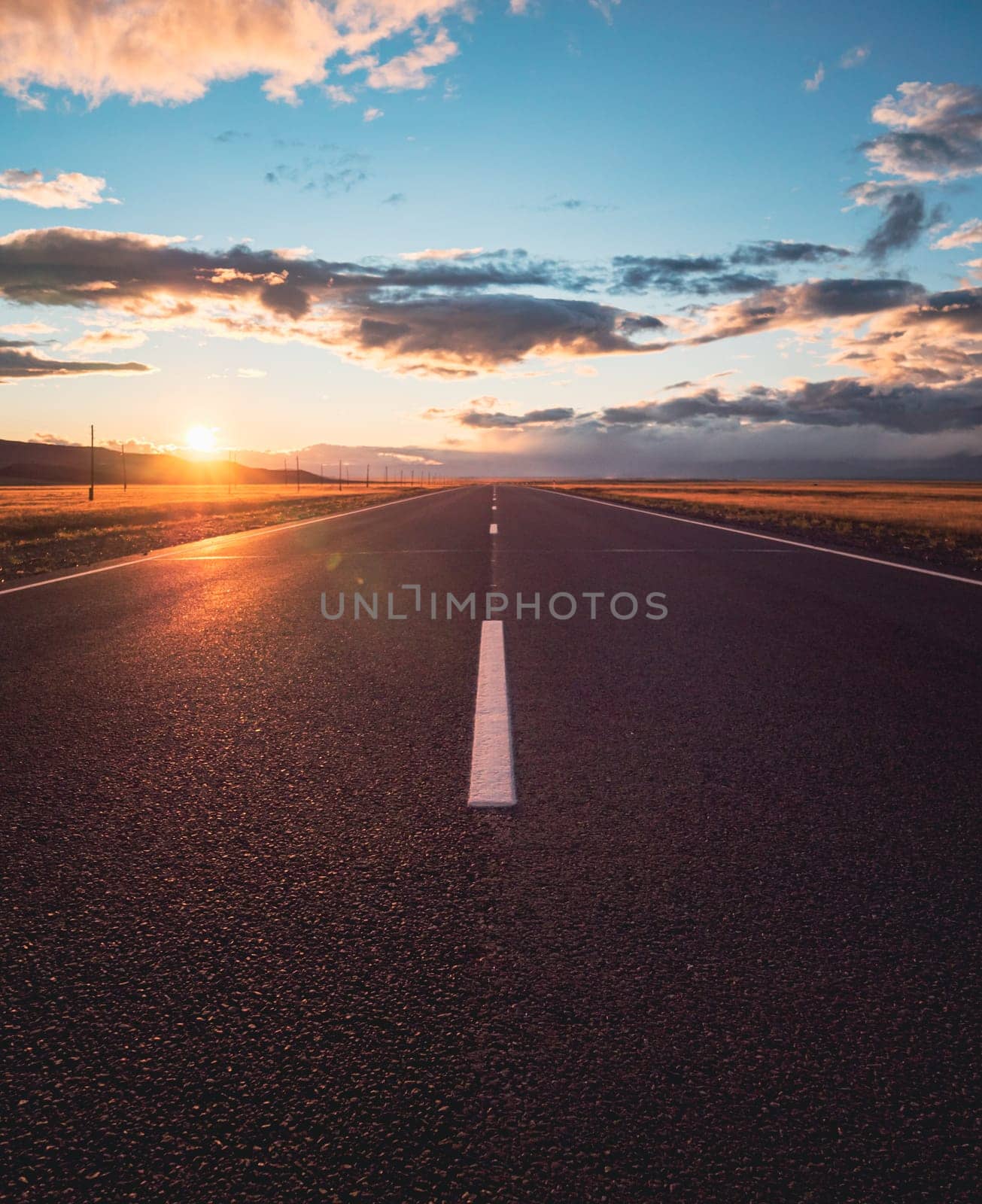 Empty intercity countryside asphalt road with the blue sky, sun and clouds on the background at sunset. Beautiful landscape