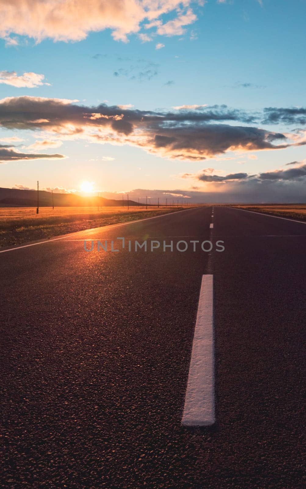Empty intercity countryside asphalt road with the blue sky, sun and clouds on the background at sunset. Beautiful landscape by Busker