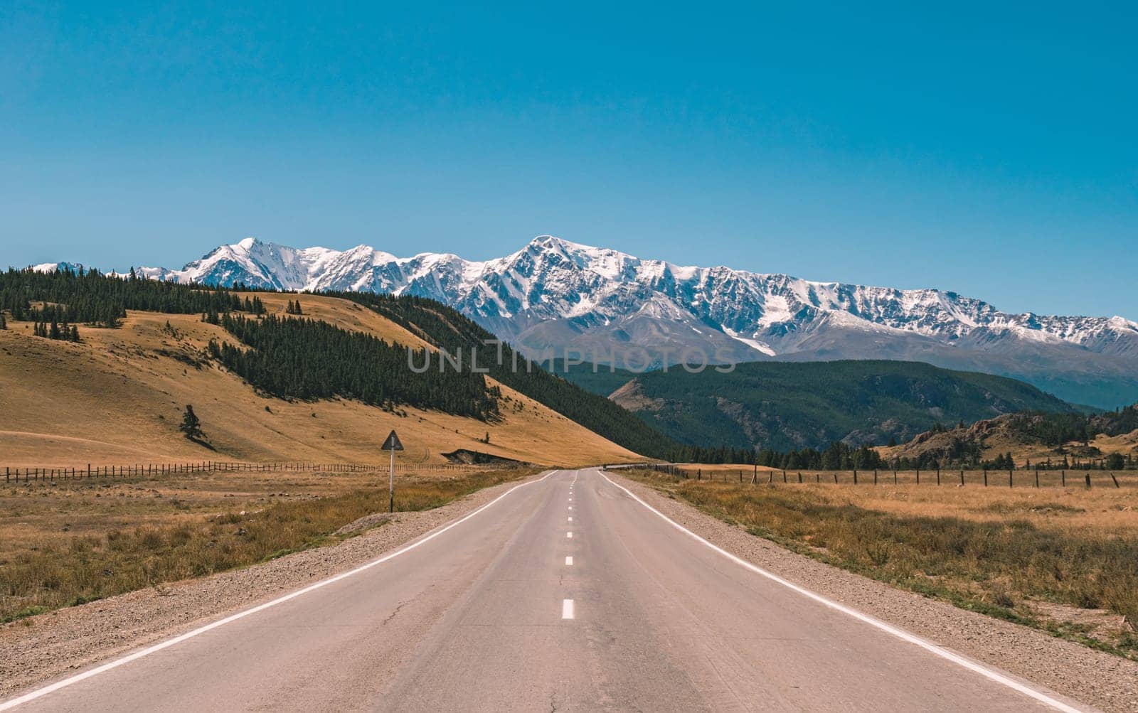 Empty asphalt road in front of huge majestic mountains with snow covered peaks. Beautiful landscape of Altay region, Russia.