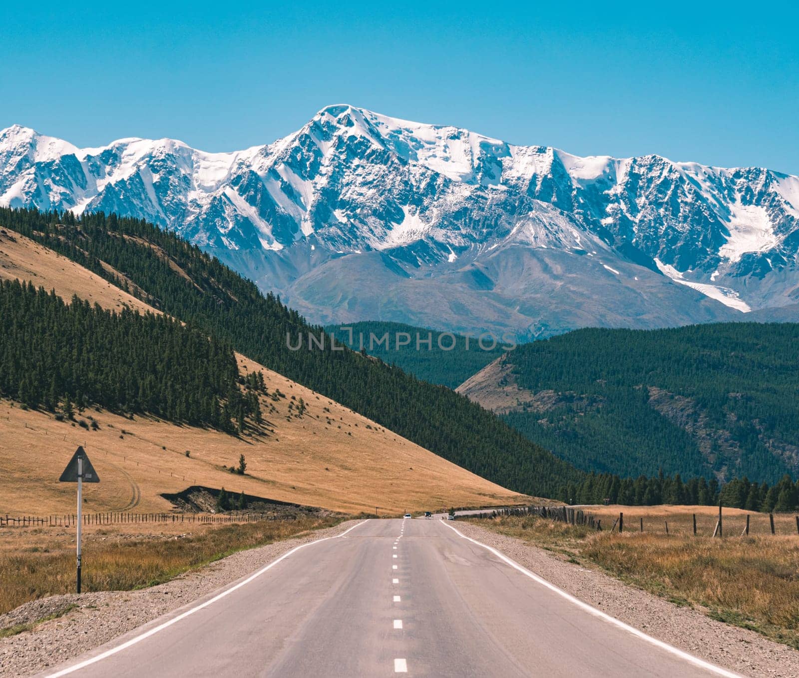 Empty asphalt road in front of huge majestic mountains with snow covered peaks. Beautiful landscape of Altay region, Russia. by Busker