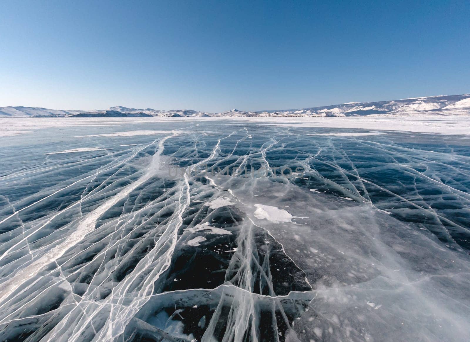 Blue snowy cracked ice of the lake Baikal. Winter landscape of frozen Baikal. Popular tourist spot