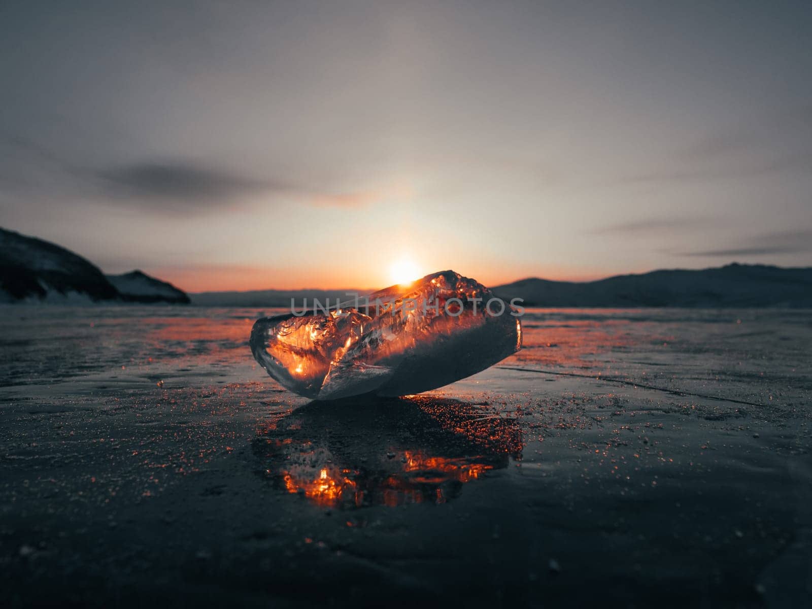 Ice crystal on the frozen surface of Lake Baikal in early morning. Sky and sun reflections on the ice surface. Amazing winter landscape. Winter tourist season at lake Baikal