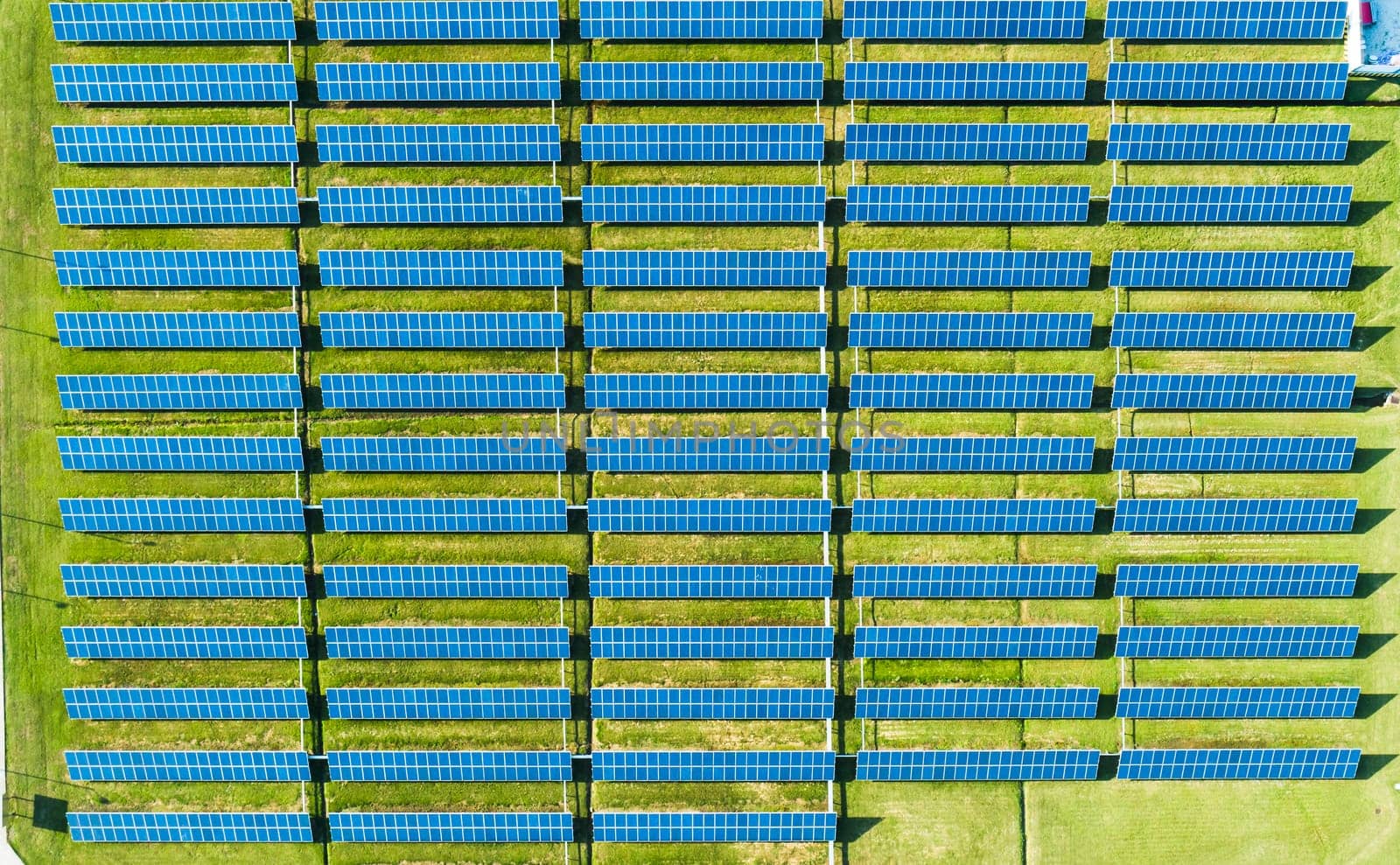 Aerial view of Solar Panels Farm with sunlight. Flying over the solar power plant at sunny day. Renewable energy power plant producing sustainable clean solar energy from the sun.