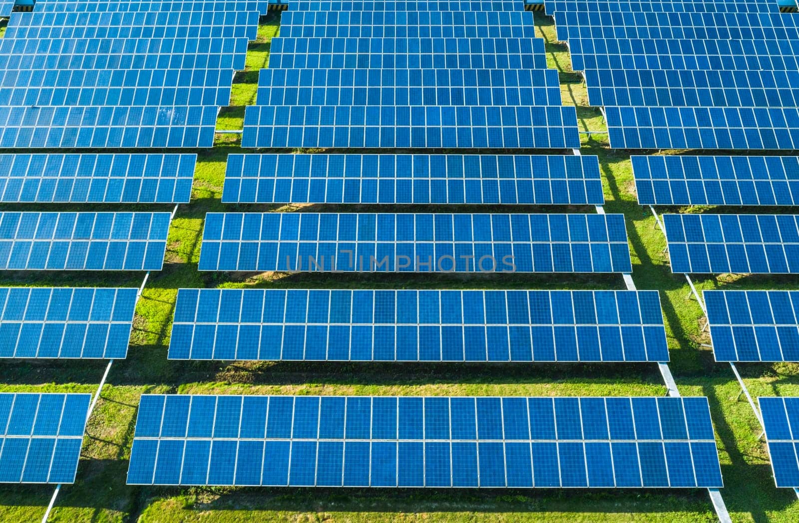 Aerial close-up view of Solar Panels Farm with sunlight. Flying over the solar power plant at sunny day. Renewable energy power plant producing sustainable clean solar energy from the sun.