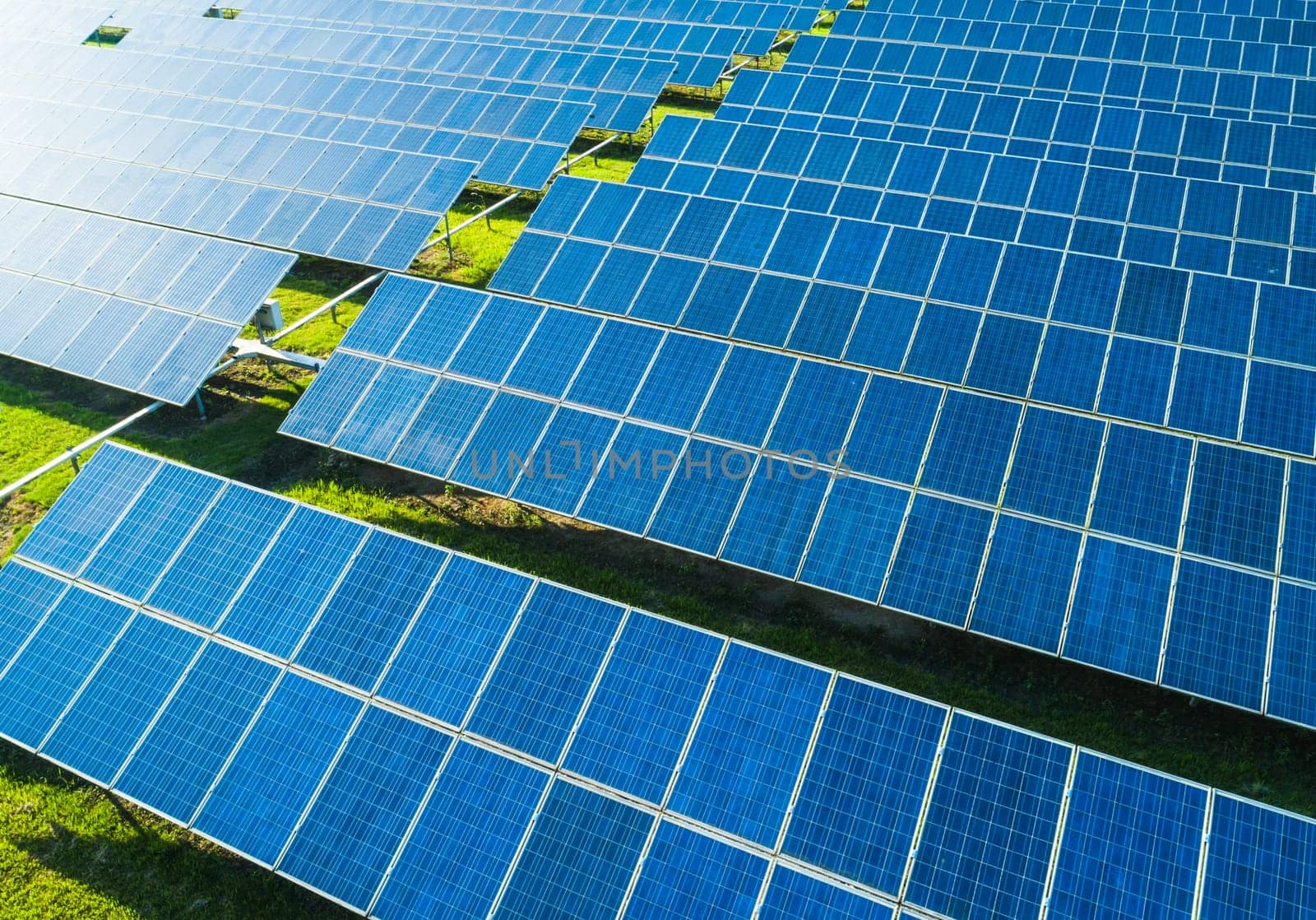 Aerial close-up view of Solar Panels Farm with sunlight. Flying over the solar power plant at sunny day. Renewable energy power plant producing sustainable clean solar energy from the sun.