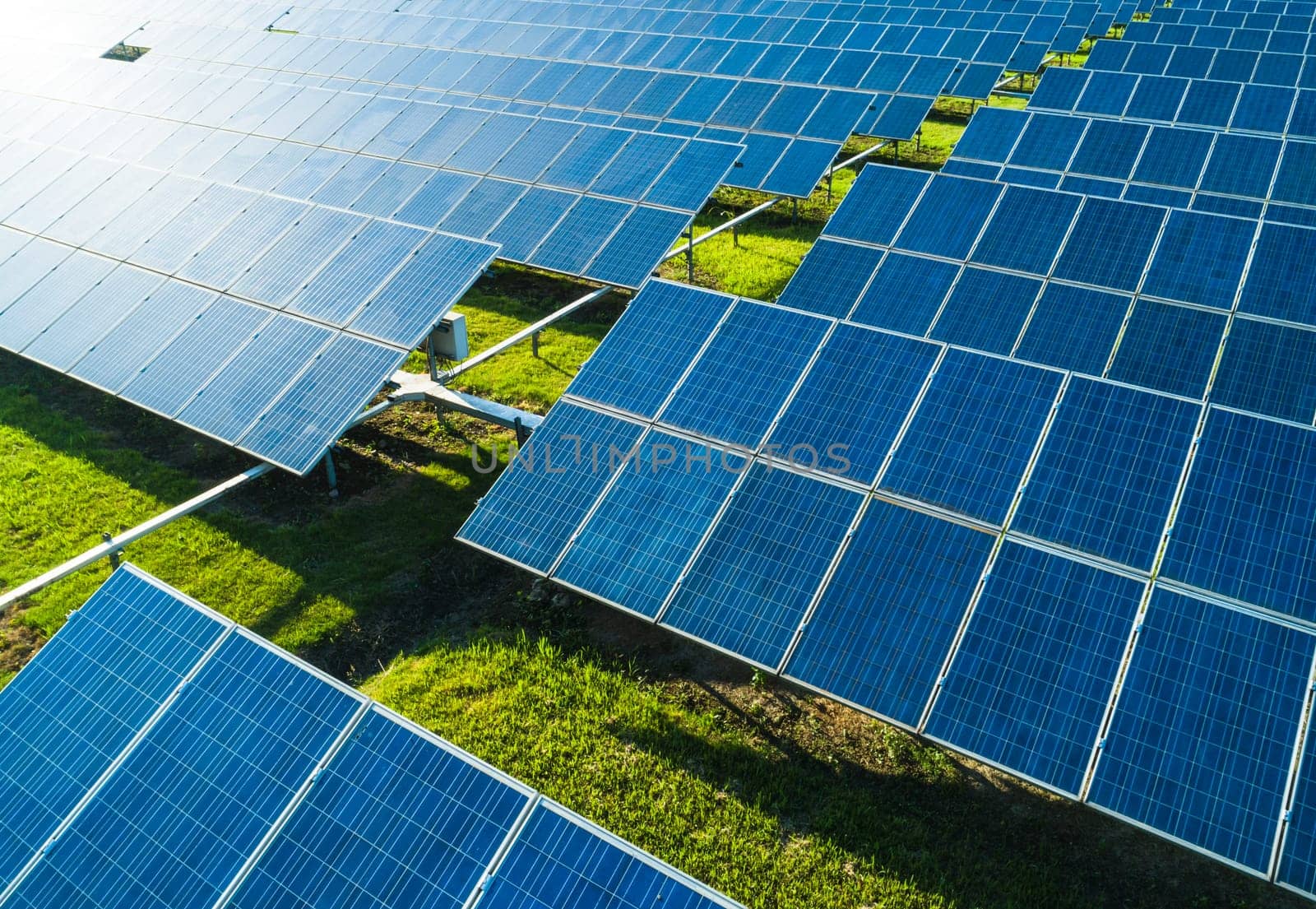 Aerial close-up view of Solar Panels Farm with sunlight. Flying over the solar power plant at sunny day. Renewable energy power plant producing sustainable clean solar energy from the sun.