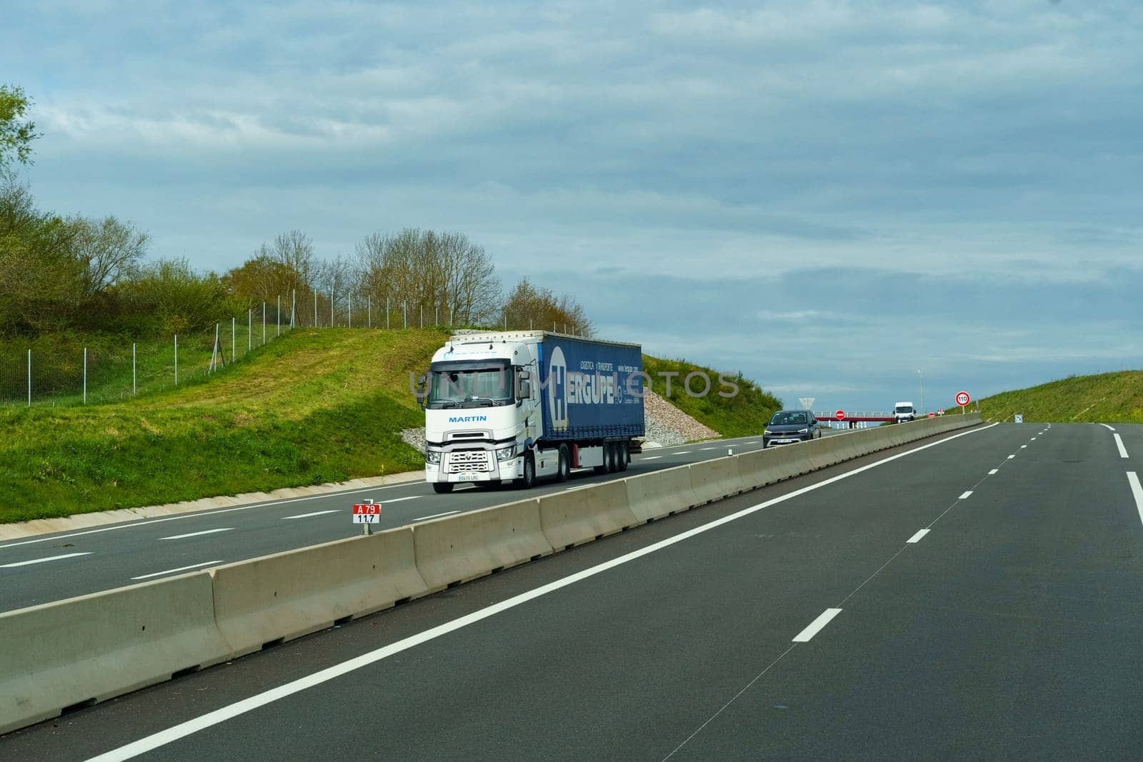 Bordeaux, France - April 26, 2023: A commercial truck is driving down a highway that runs alongside a vibrant green hillside on a sunny day.