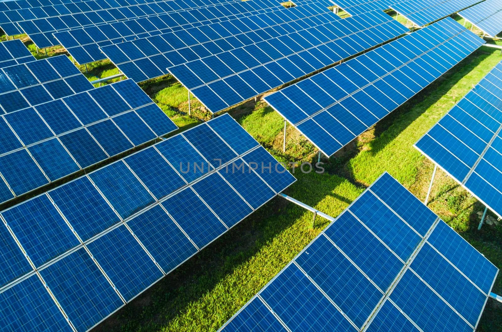 Aerial close-up view of Solar Panels Farm with sunlight. Flying over the solar power plant at sunny day. Renewable energy power plant producing sustainable clean solar energy from the sun.