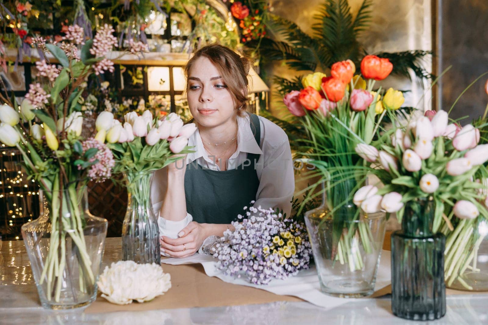 A woman in her florist shop collects bouquets of flowers. The concept of a small business. Bouquets of tulips for the holiday on March 8