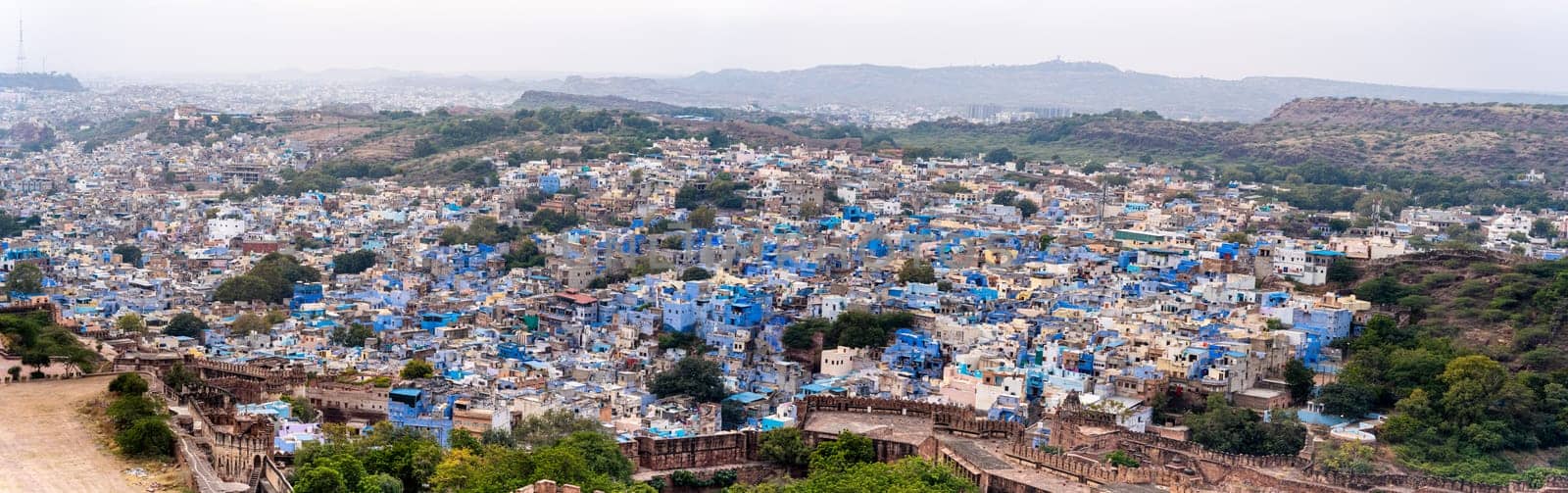 Panoramic aerial drone shot showing jodhpur blue city cityscape showing traditional houses in middle of aravalli with colorful densely packed houses by Shalinimathur