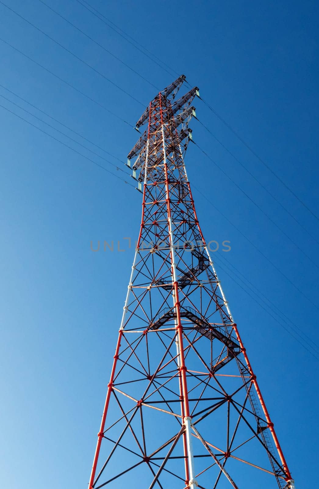 Bottom view of a high-voltage electricity pylon against blue sky at sunny day. High-voltage power transmission tower. Power engineering.