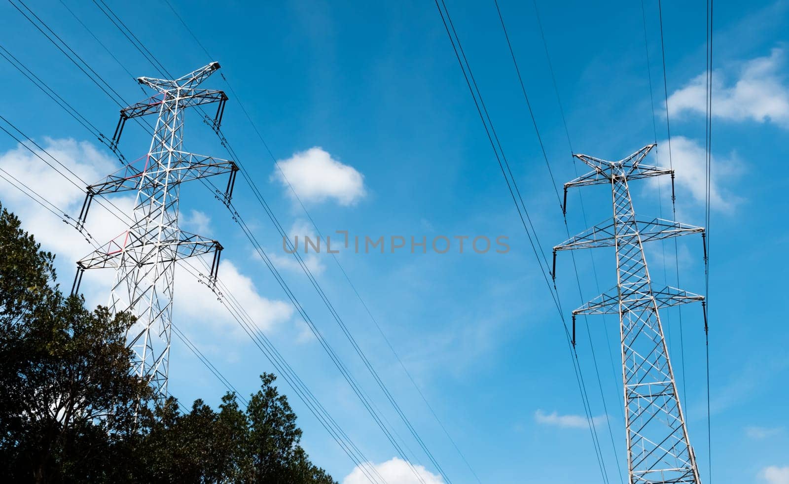 Bottom view of a high-voltage electricity pylons against blue sky with clouds at sunny day. High-voltage power transmission towers. Power engineering.