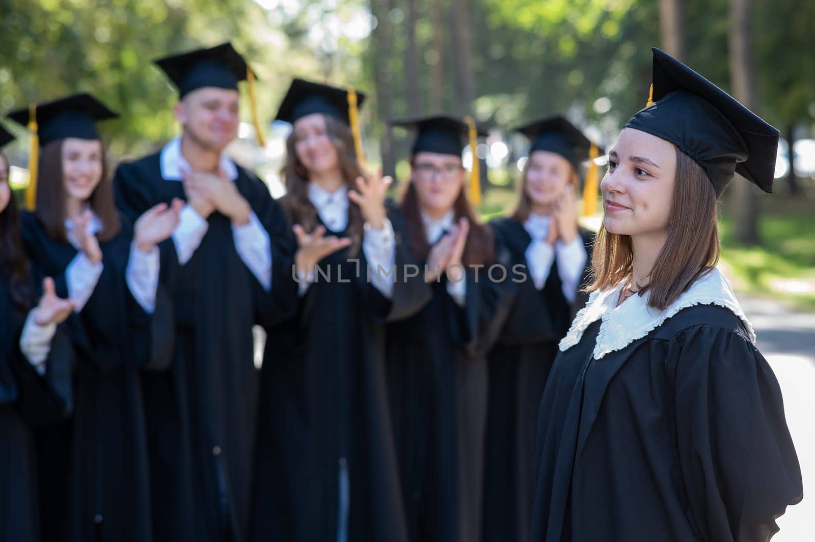 Group of happy students in graduation gowns outdoors. A young girl in the foreground. by mrwed54