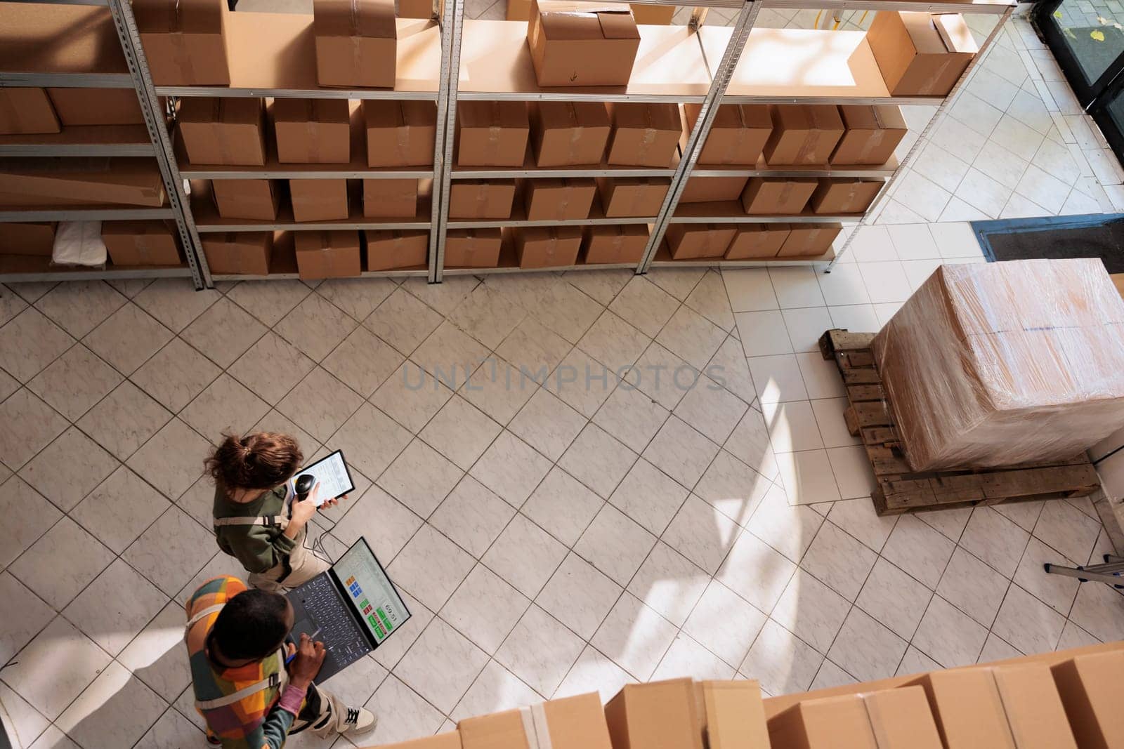 Diverse storage room workers tracking customers orders, checking warehouse logistics using laptop computer. Supervisor preparing packages for delivery with storehouse manager. Top view concept