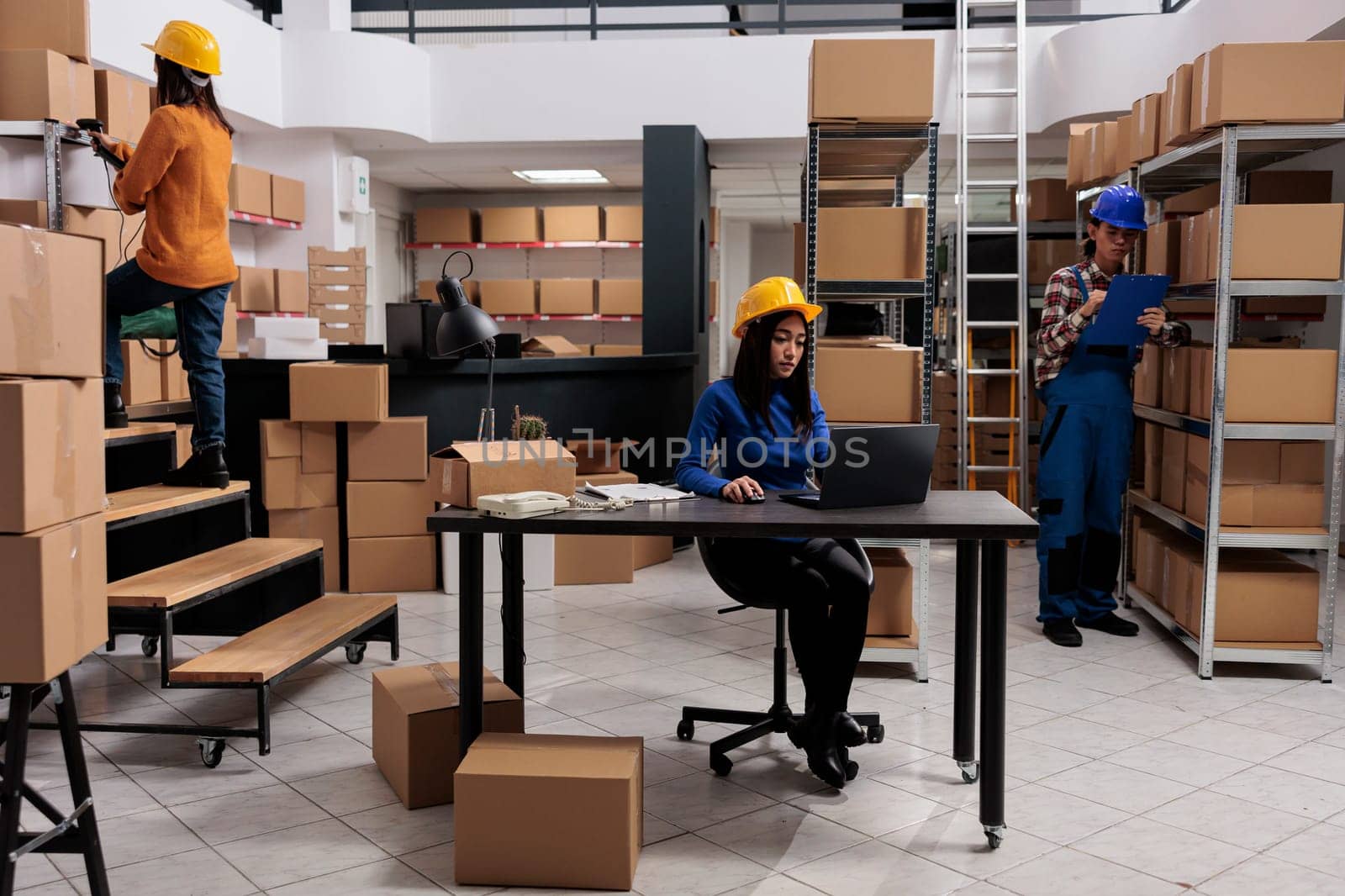 Asian delivery service employees team working in warehouse together. Storehouse workers tracking parchel shipment on laptop, searching parcel on rack and doing inventory management