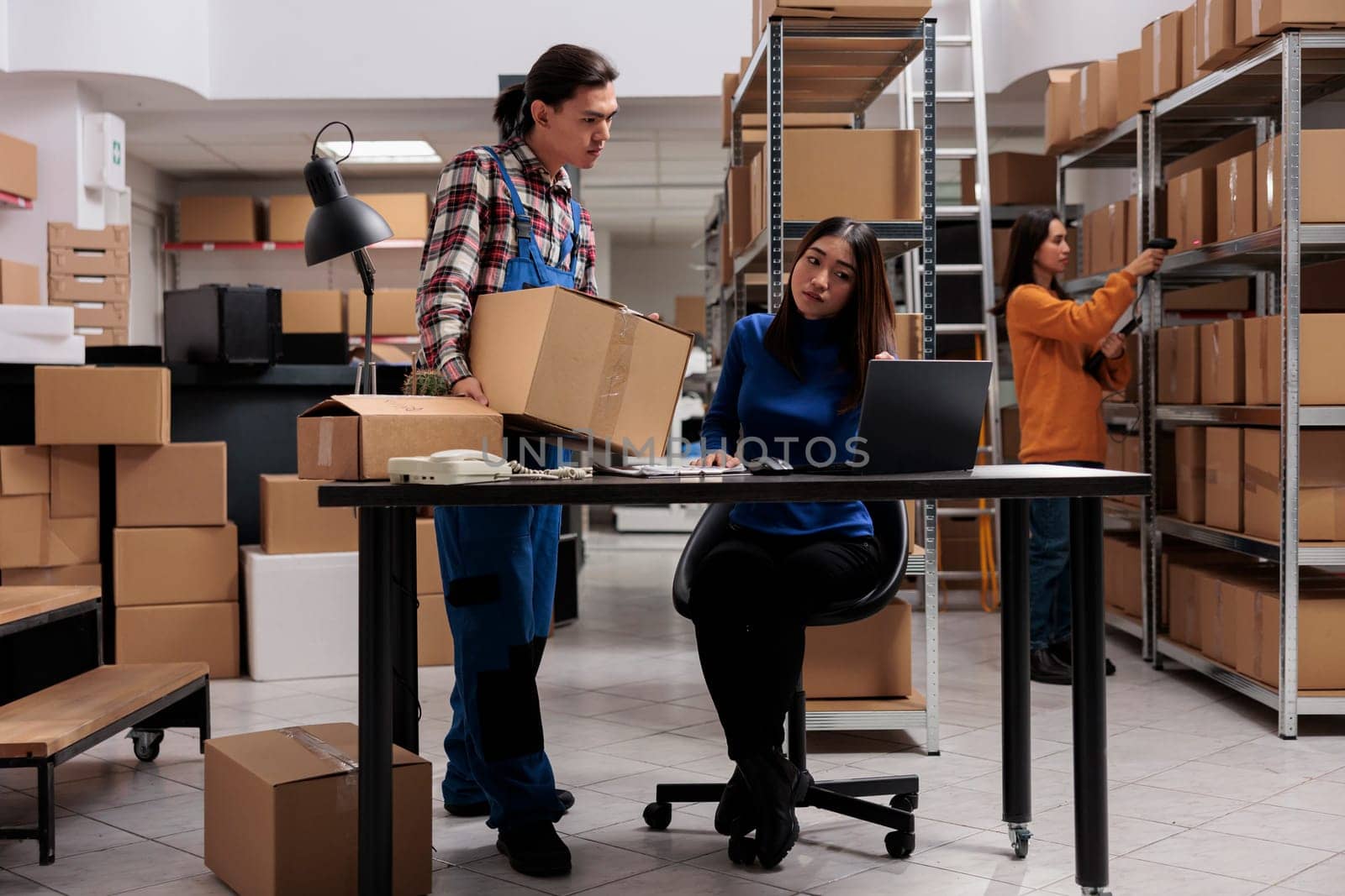 Warehouse asian operators team managing package delivery in storage room. Storehouse worker holding parcel ready for transportation and woman coworker scheduling shipment