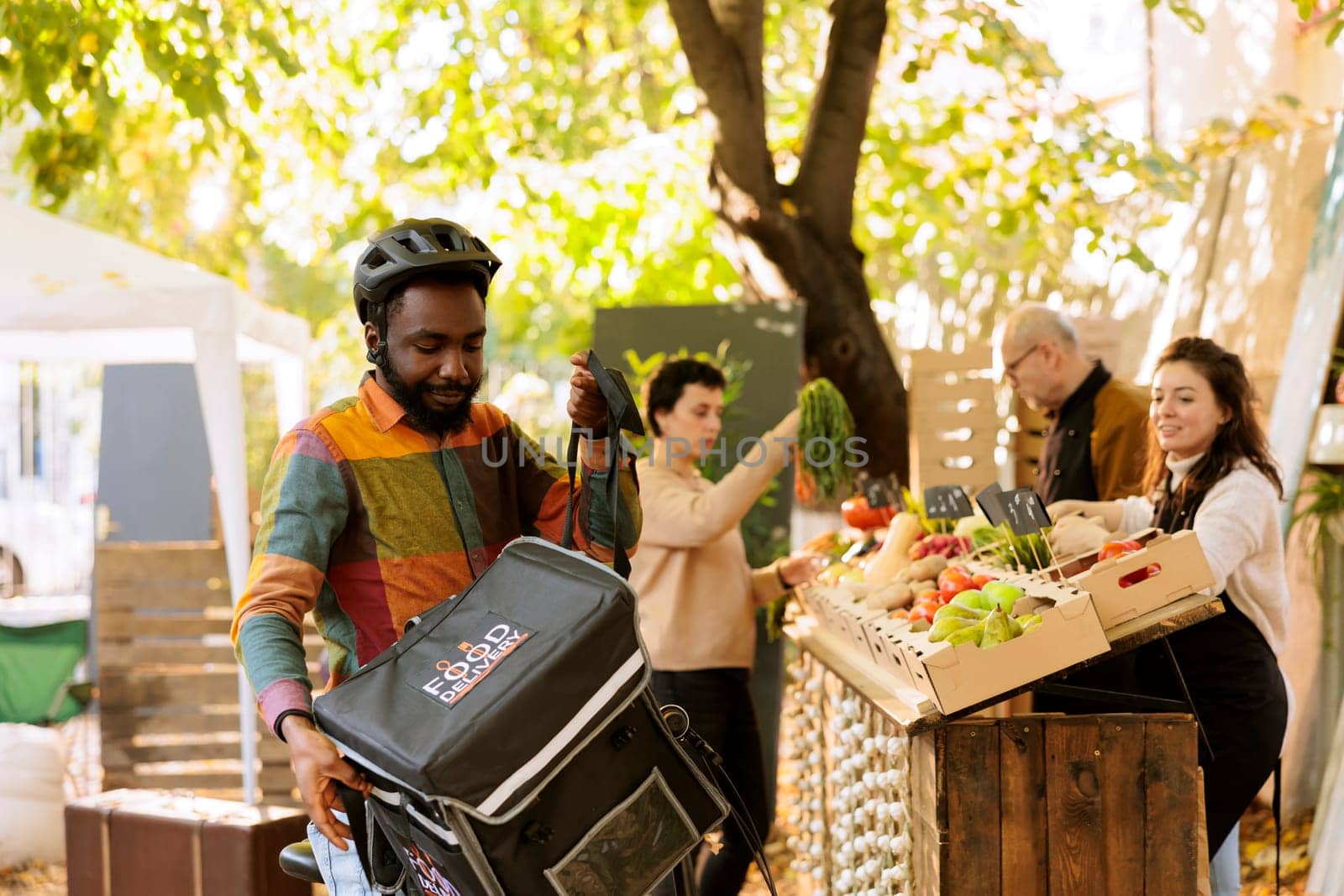 Black deliveryman holding thermal bag, waiting for order at local food market. Farmers delivering fresh organic fruits and vegetables to customers using african american courier with helmet.
