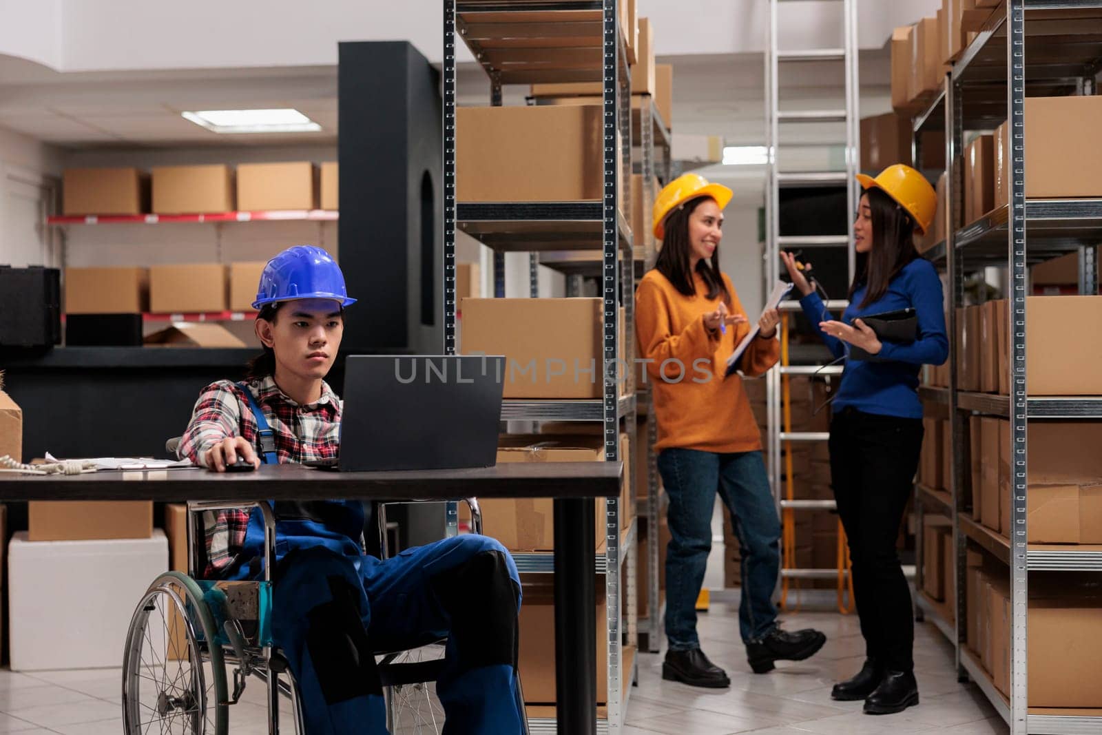 Warehouse worker in wheelchair planning delivery on laptop by DCStudio