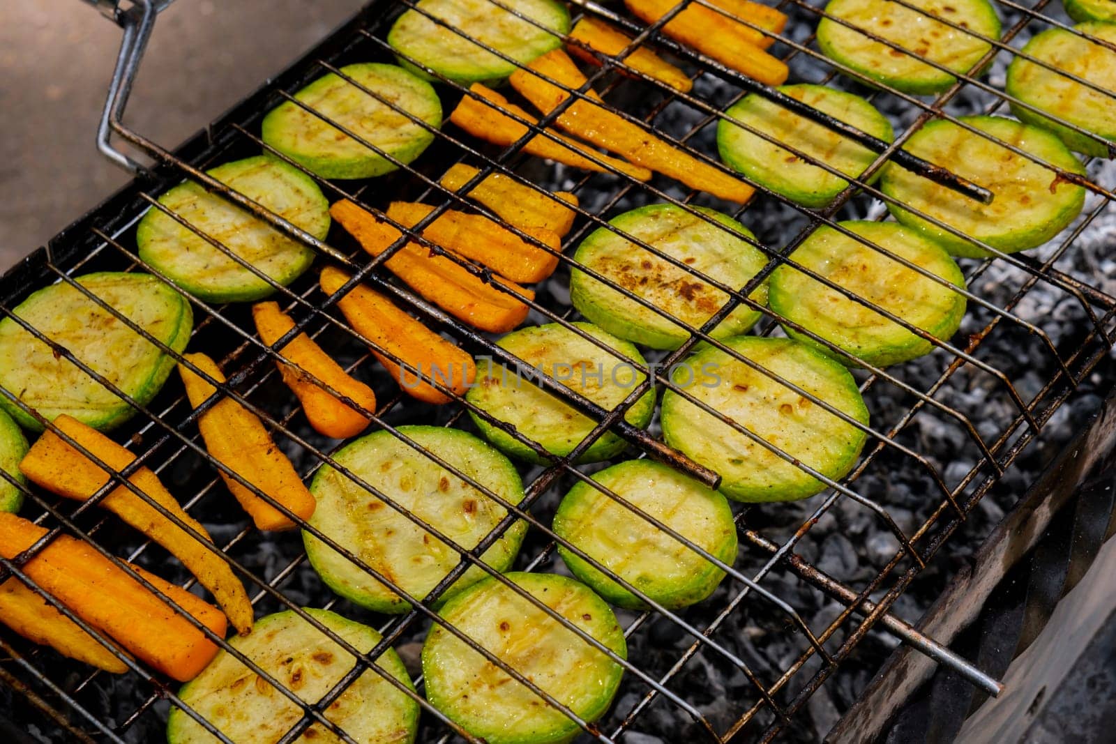 Chopped zucchini and carrots roasting on fire seasoned with aroma herbs and spices. Delicious fresh vegetables grilling on barbecue smoker grid. Diet vegan bbq. Outdoor recreation by anna_stasiia