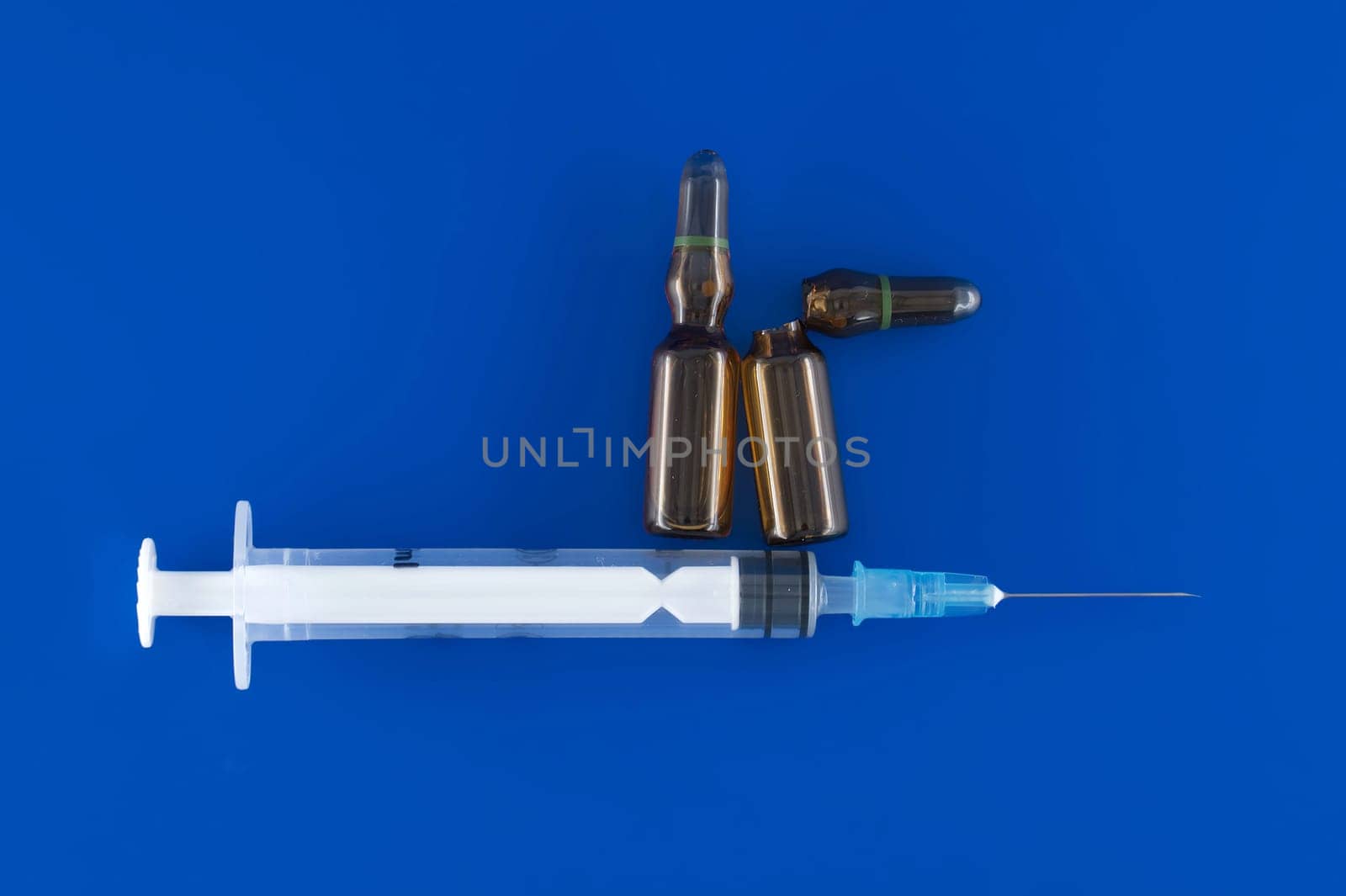 Needle, syringe and two brown vaccine ampules appearing ready for use against a blue background, medical treatment and vaccination