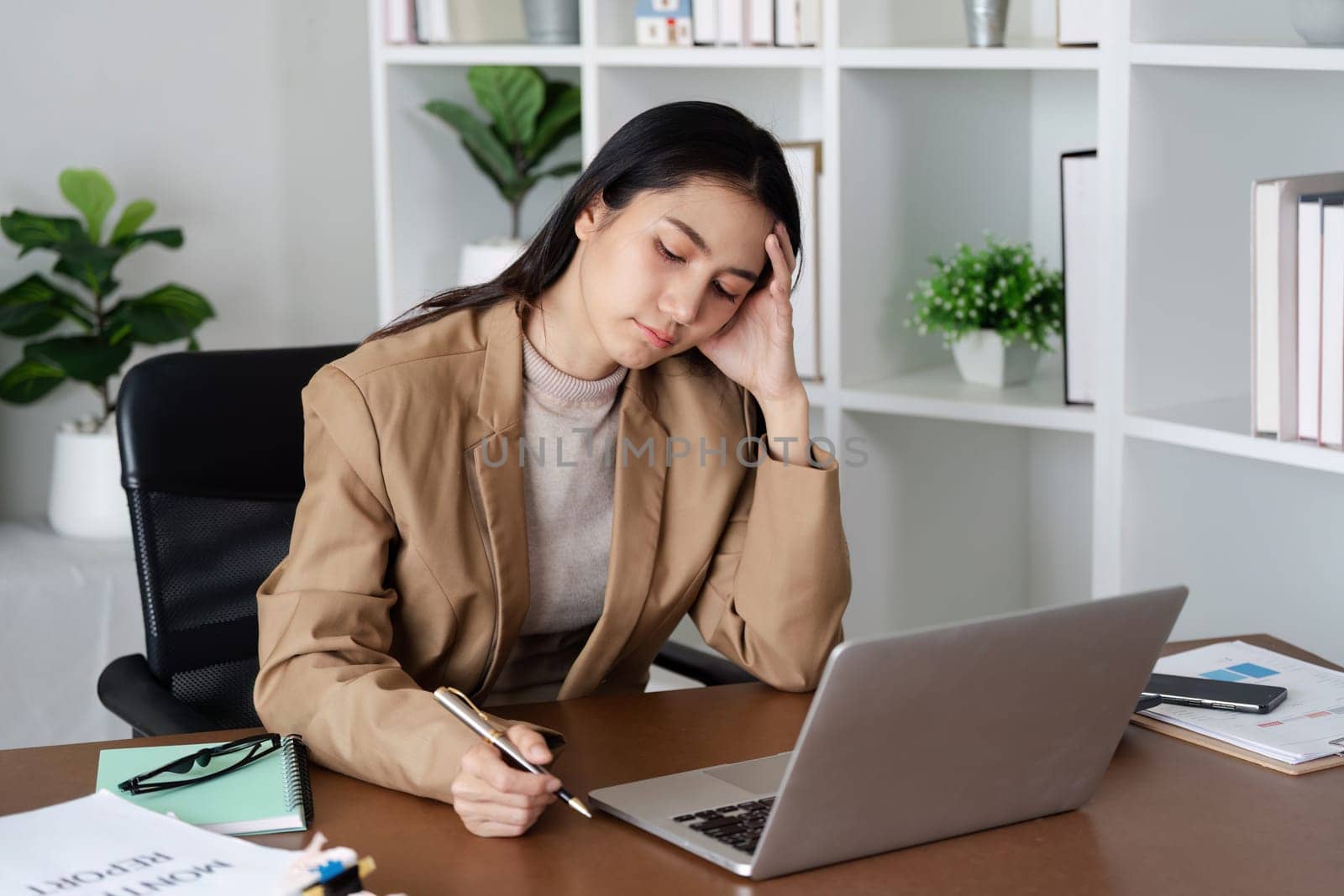 A woman is sitting at a desk with a laptop and a pen. She is writing something on a piece of paper