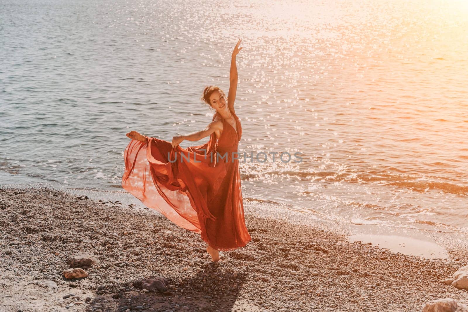 Woman red dress sea. Female dancer in a long red dress posing on a beach with rocks on sunny day. Girl on the nature on blue sky background