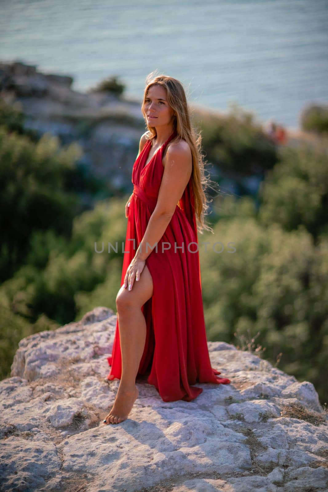 Woman sunset sea red dress, back view a happy beautiful sensual woman in a red long dress posing on a rock high above the sea on sunset. by Matiunina