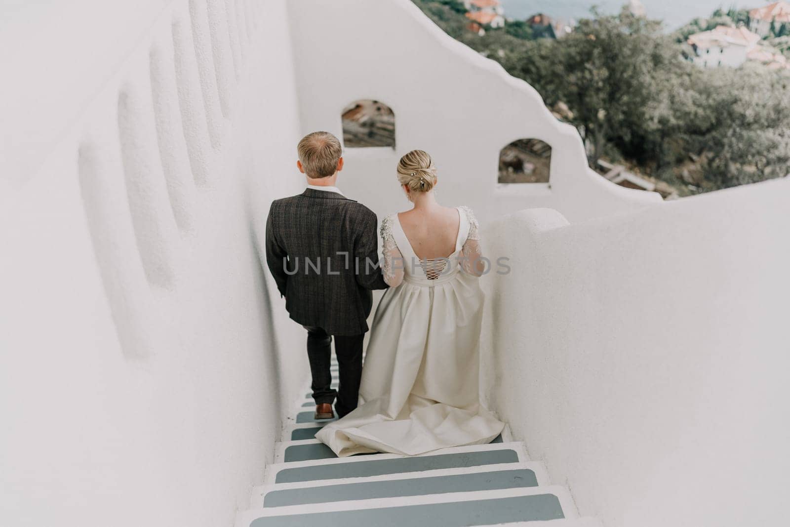 A bride and groom are walking down a white staircase. The bride is wearing a white dress and the groom is wearing a suit